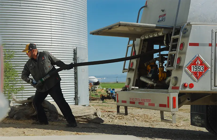 Senergy Petroleum driver pulling fuel hose from tanker truck next to storage tank