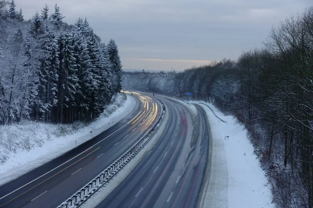 a snowy road with cars driving and trees on the side of the road covered in snow